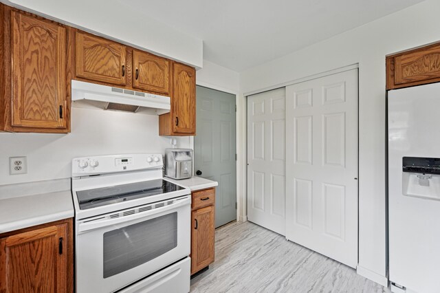 kitchen with white appliances, under cabinet range hood, brown cabinetry, light countertops, and light wood-style floors