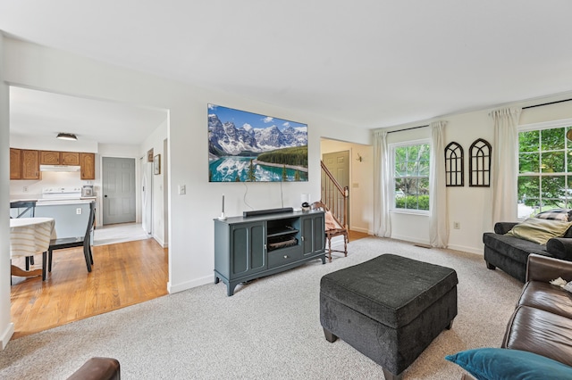 living room with stairway, healthy amount of natural light, baseboards, and light colored carpet