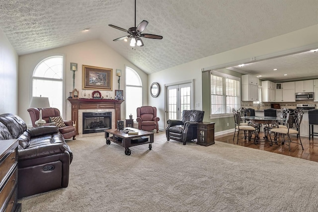 living area with a textured ceiling, ceiling fan, healthy amount of natural light, vaulted ceiling, and a tile fireplace