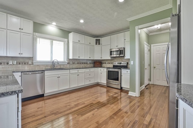 kitchen featuring appliances with stainless steel finishes, a sink, crown molding, white cabinets, and a textured ceiling