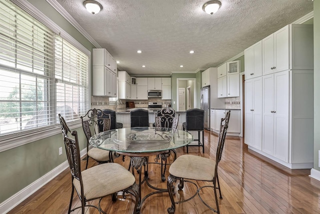 dining area with a textured ceiling, ornamental molding, light wood-type flooring, baseboards, and recessed lighting