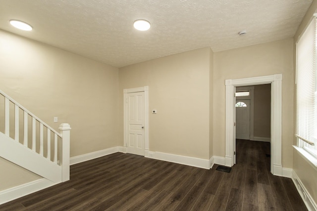 empty room with dark wood-style flooring, plenty of natural light, baseboards, and a textured ceiling