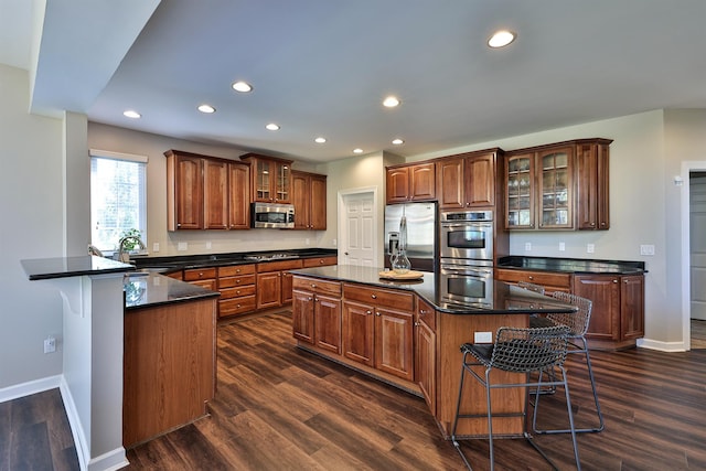kitchen featuring appliances with stainless steel finishes, a sink, dark countertops, baseboards, and a kitchen bar