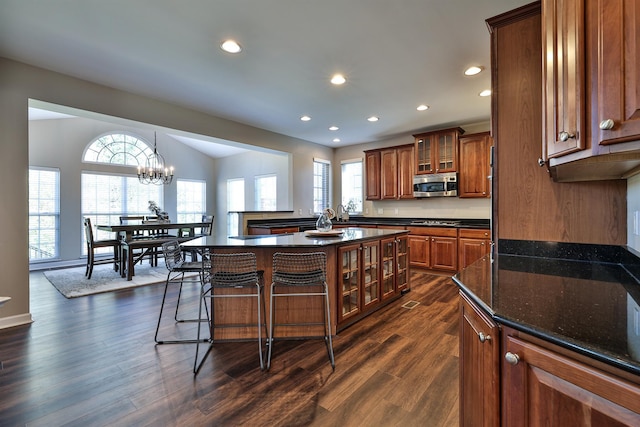 kitchen featuring stainless steel microwave, brown cabinets, recessed lighting, glass insert cabinets, and a breakfast bar area