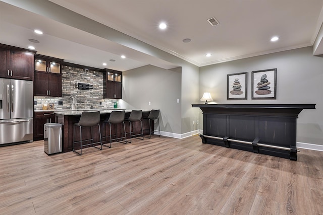 indoor wet bar featuring stainless steel refrigerator with ice dispenser, ornamental molding, baseboards, recessed lighting, and light wood-style flooring