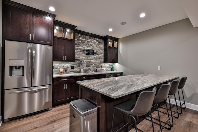 kitchen with stainless steel fridge with ice dispenser, a kitchen bar, light wood finished floors, decorative backsplash, and light stone counters