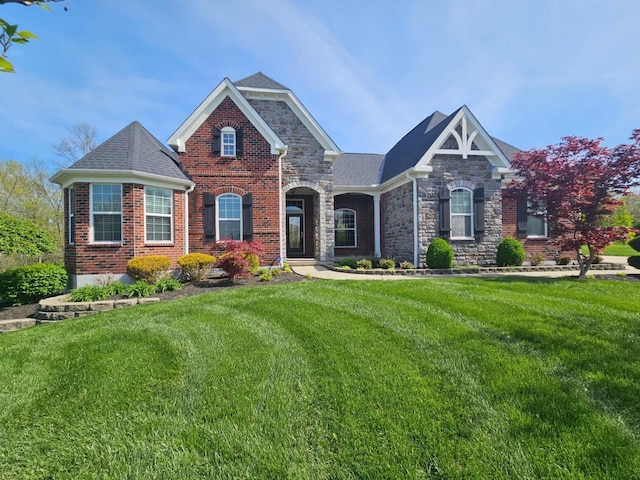 view of front of house with stone siding, a front yard, brick siding, and roof with shingles