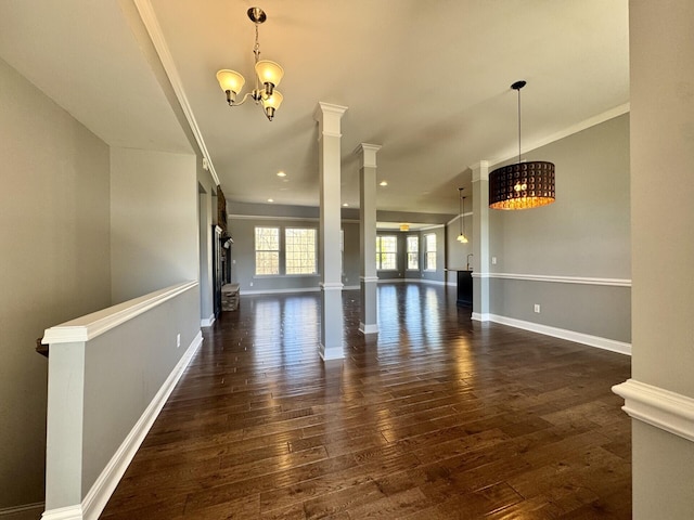 unfurnished living room featuring dark wood-type flooring, decorative columns, a chandelier, baseboards, and ornamental molding