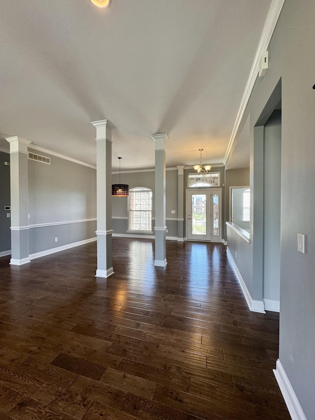 unfurnished living room featuring ornate columns, ornamental molding, dark wood-style floors, baseboards, and a chandelier