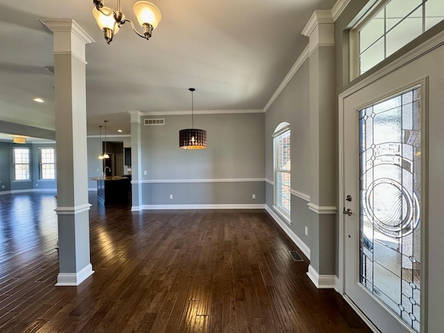 entrance foyer with a chandelier, ornate columns, dark wood-type flooring, baseboards, and crown molding