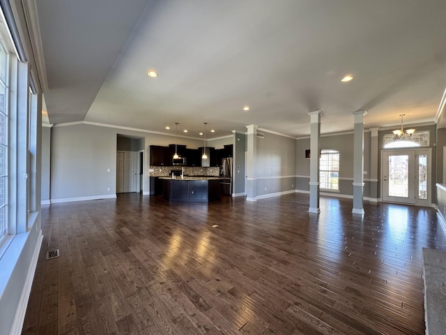 unfurnished living room with decorative columns, crown molding, dark wood-type flooring, baseboards, and recessed lighting