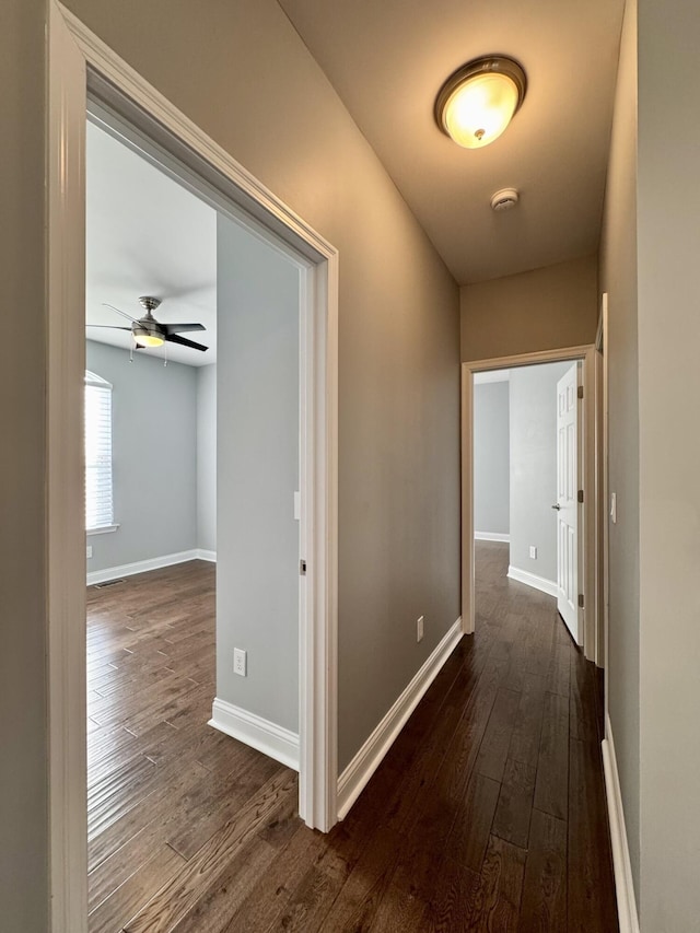 corridor featuring dark wood-style flooring and baseboards