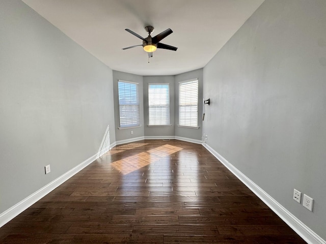 empty room featuring dark wood-style flooring, a ceiling fan, and baseboards
