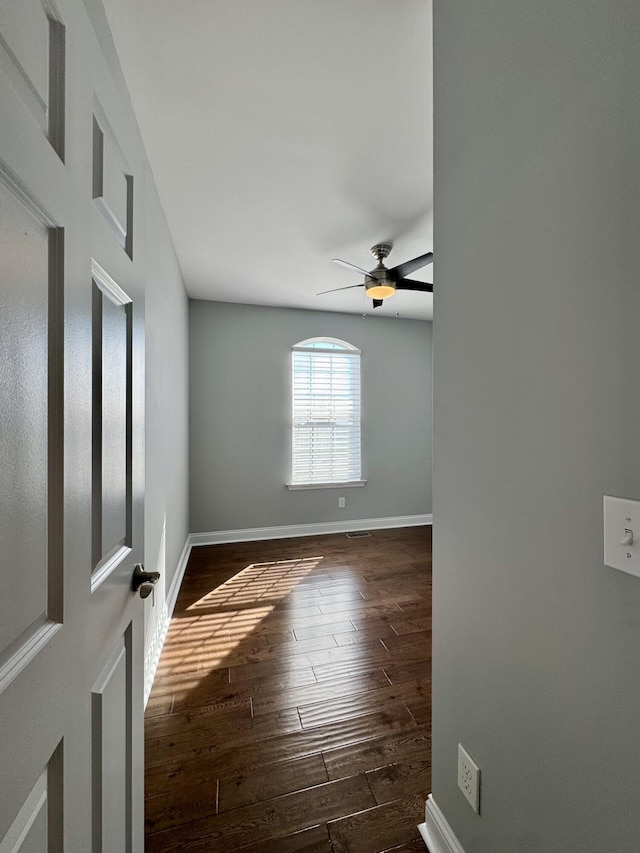 unfurnished room with dark wood-style flooring, ceiling fan, and baseboards