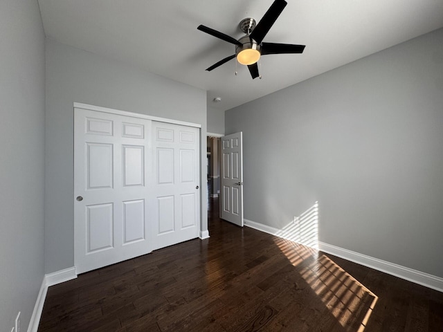 unfurnished bedroom featuring dark wood-type flooring, baseboards, a closet, and ceiling fan