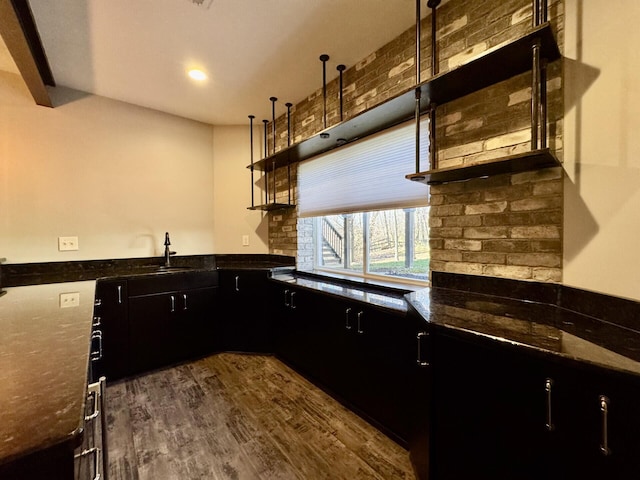 kitchen featuring dark wood-style floors, dark cabinets, dark stone counters, a sink, and open shelves