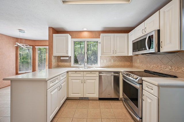 kitchen with appliances with stainless steel finishes, a peninsula, light tile patterned floors, white cabinetry, and a textured ceiling