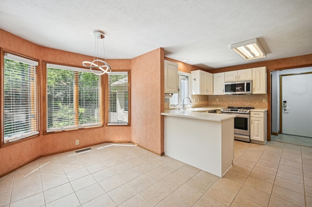 kitchen with appliances with stainless steel finishes, light countertops, tasteful backsplash, light tile patterned floors, and a textured ceiling