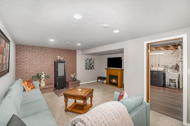living room featuring washer / clothes dryer, a lit fireplace, recessed lighting, light carpet, and brick wall
