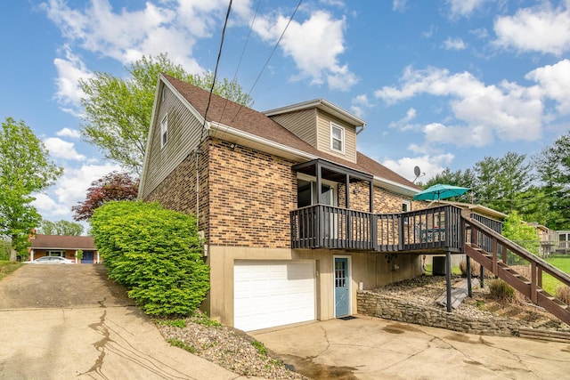 view of side of property featuring brick siding, concrete driveway, an attached garage, a deck, and stairway