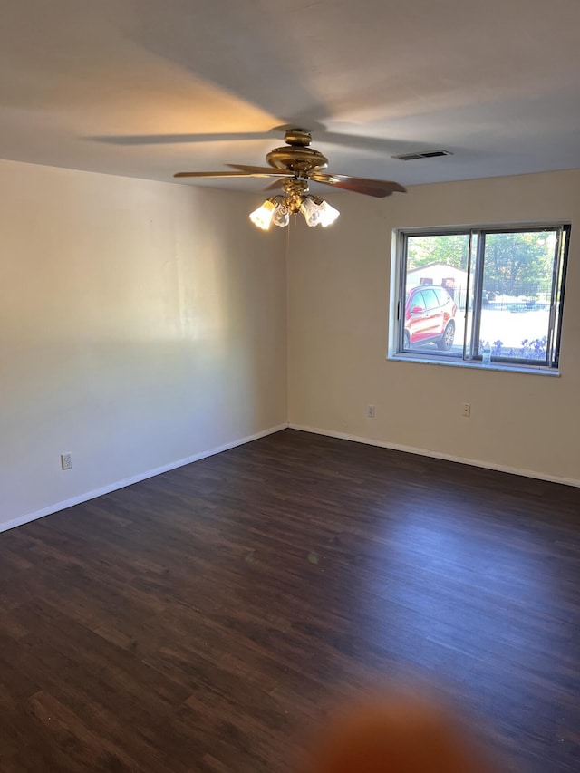 spare room featuring dark wood-style floors, a ceiling fan, and baseboards