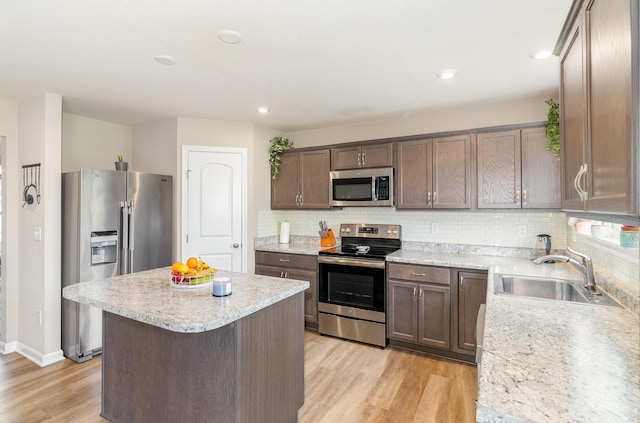 kitchen featuring appliances with stainless steel finishes, a sink, light wood finished floors, light countertops, and decorative backsplash