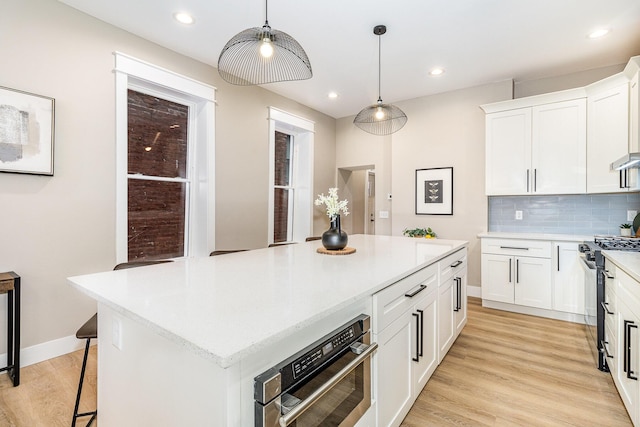 1102 Lee St, Covington, KY 41011 - kitchen featuring stainless steel appliances, a center island, light wood finished floors, white cabinetry, and backsplash