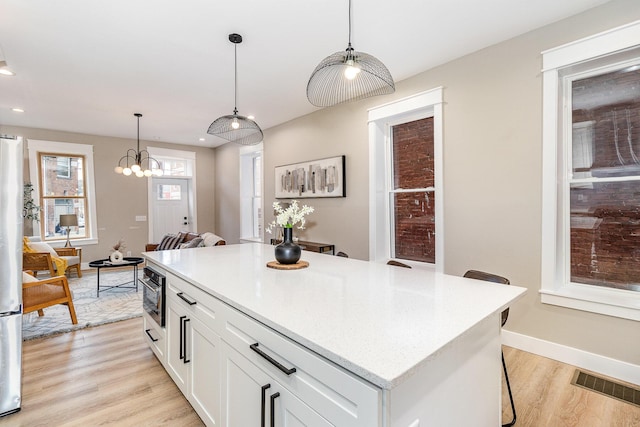 1102 Lee St, Covington, KY 41011 - kitchen featuring light wood-type flooring, pendant lighting, a kitchen bar, white cabinetry, and light countertops
