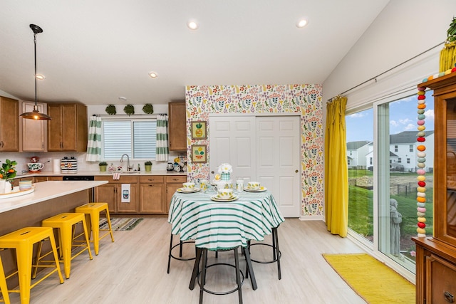 kitchen featuring a sink, plenty of natural light, brown cabinets, light wood-type flooring, and wallpapered walls