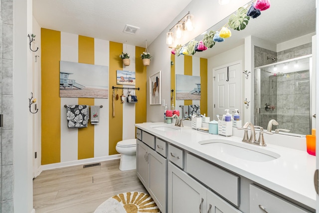 bathroom featuring a stall shower, wood finished floors, double vanity, baseboards, and toilet