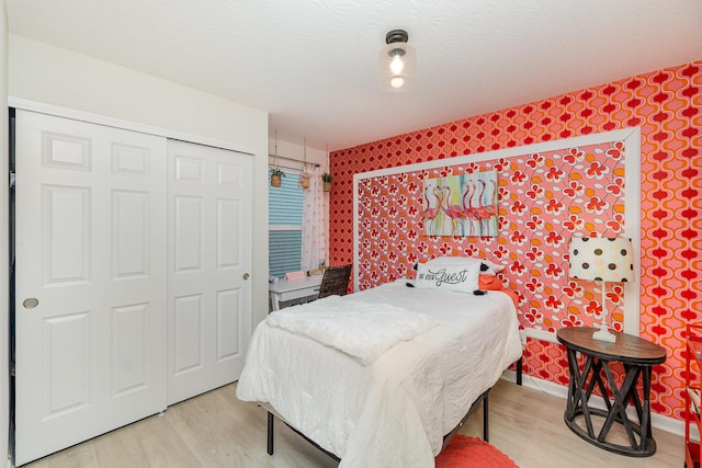 bedroom featuring wood finished floors, wallpapered walls, and a closet