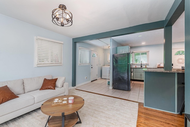 living room featuring washer / dryer, light wood-style floors, a chandelier, and baseboards