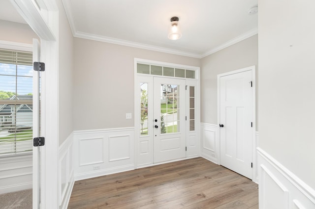 foyer entrance with crown molding, wainscoting, light wood-style floors, and a decorative wall