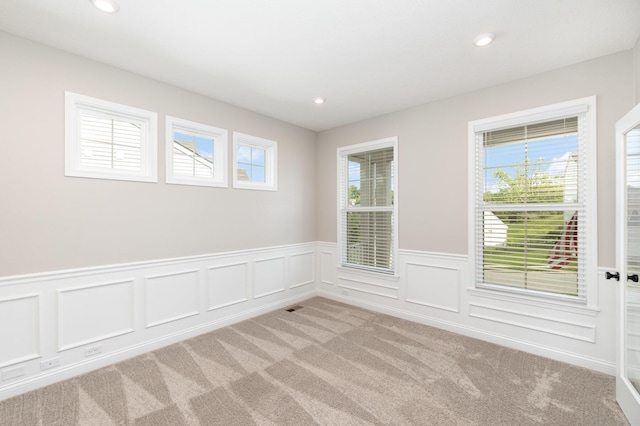 spare room featuring light colored carpet, a wainscoted wall, recessed lighting, and a decorative wall