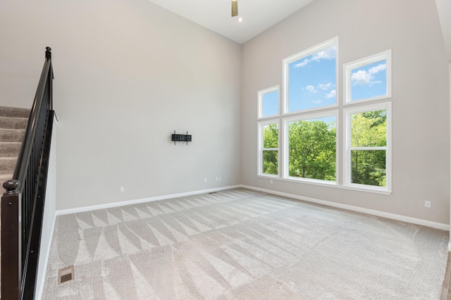 carpeted spare room with baseboards, ceiling fan, and a towering ceiling