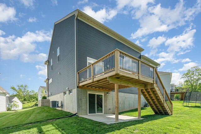 rear view of house featuring central AC unit, a trampoline, a lawn, a patio, and a deck