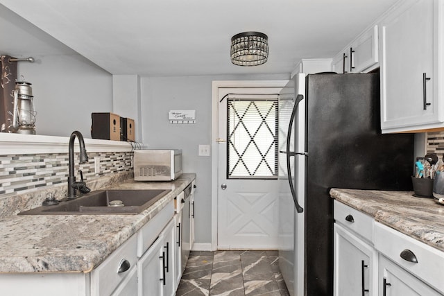 kitchen with white microwave, a sink, tasteful backsplash, freestanding refrigerator, and white cabinetry