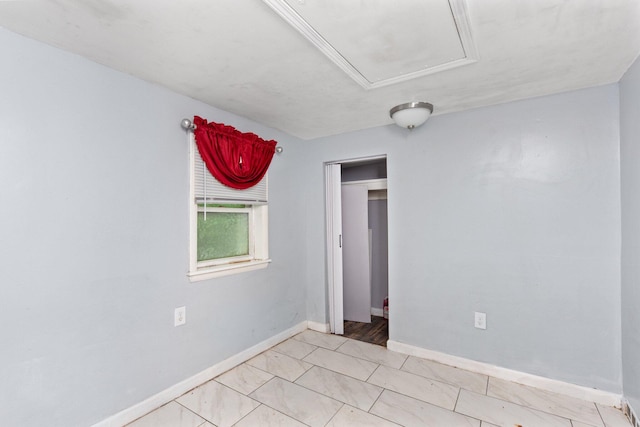 empty room with attic access and baseboards