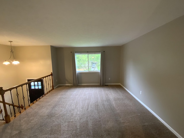 carpeted spare room featuring baseboards and a chandelier