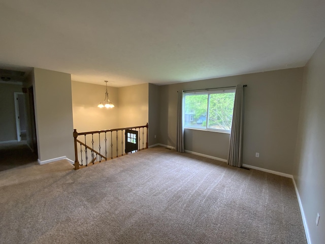 carpeted empty room featuring a chandelier and baseboards