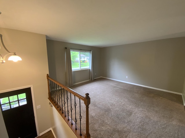 carpeted spare room featuring baseboards, a chandelier, and stairs