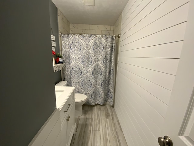 bathroom with toilet, vanity, a shower with shower curtain, and wood walls