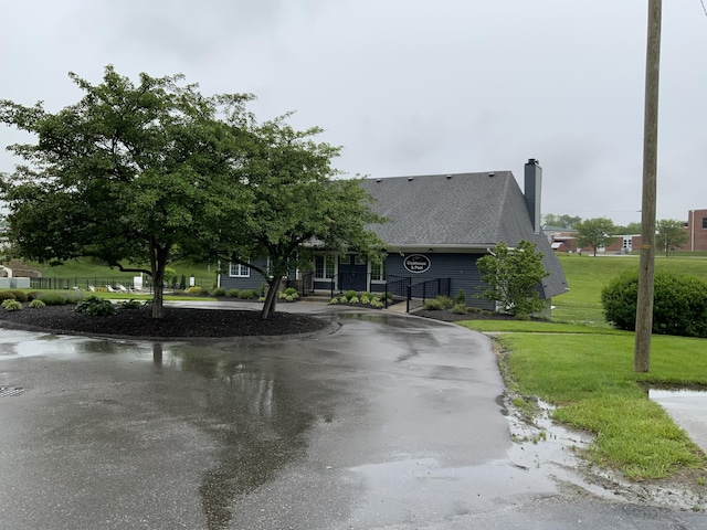 view of front of home featuring a chimney, a front yard, roof with shingles, and curved driveway