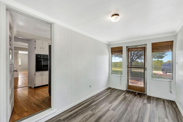 empty room featuring wood finished floors, crown molding, and baseboards