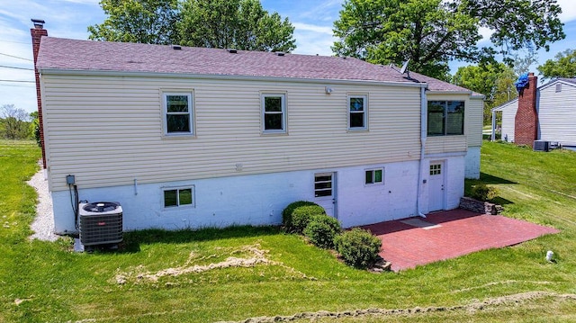 rear view of house with central AC unit, a patio, a lawn, roof with shingles, and a chimney