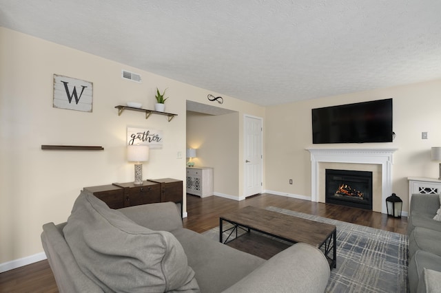 living room with wood finished floors, a warm lit fireplace, baseboards, and a textured ceiling
