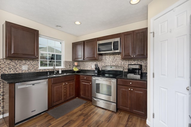 kitchen featuring stainless steel appliances, a sink, dark wood finished floors, decorative backsplash, and recessed lighting