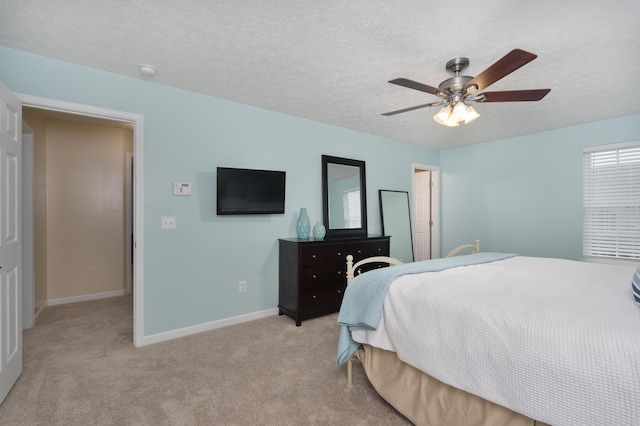 bedroom with light carpet, a textured ceiling, baseboards, and a ceiling fan