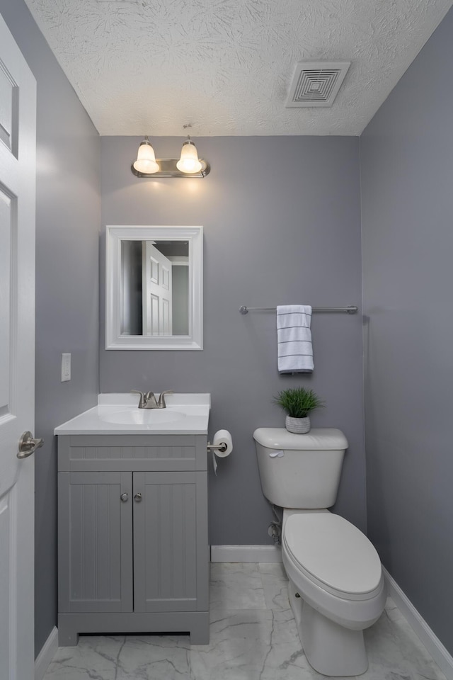 half bathroom featuring marble finish floors, toilet, baseboards, vanity, and a textured ceiling