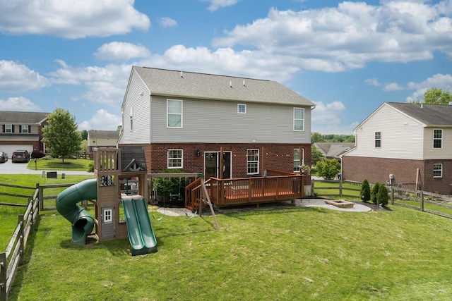 rear view of property with a playground, a deck, brick siding, and a fire pit